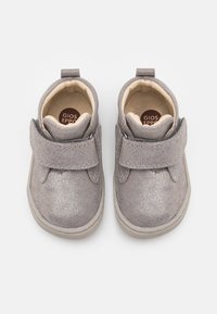 Botas de tobillo de ante gris con una textura suave, que cuentan con una correa de Velcro y un forro interior en tono marrón claro. Puntera redondeada y suela de color claro.