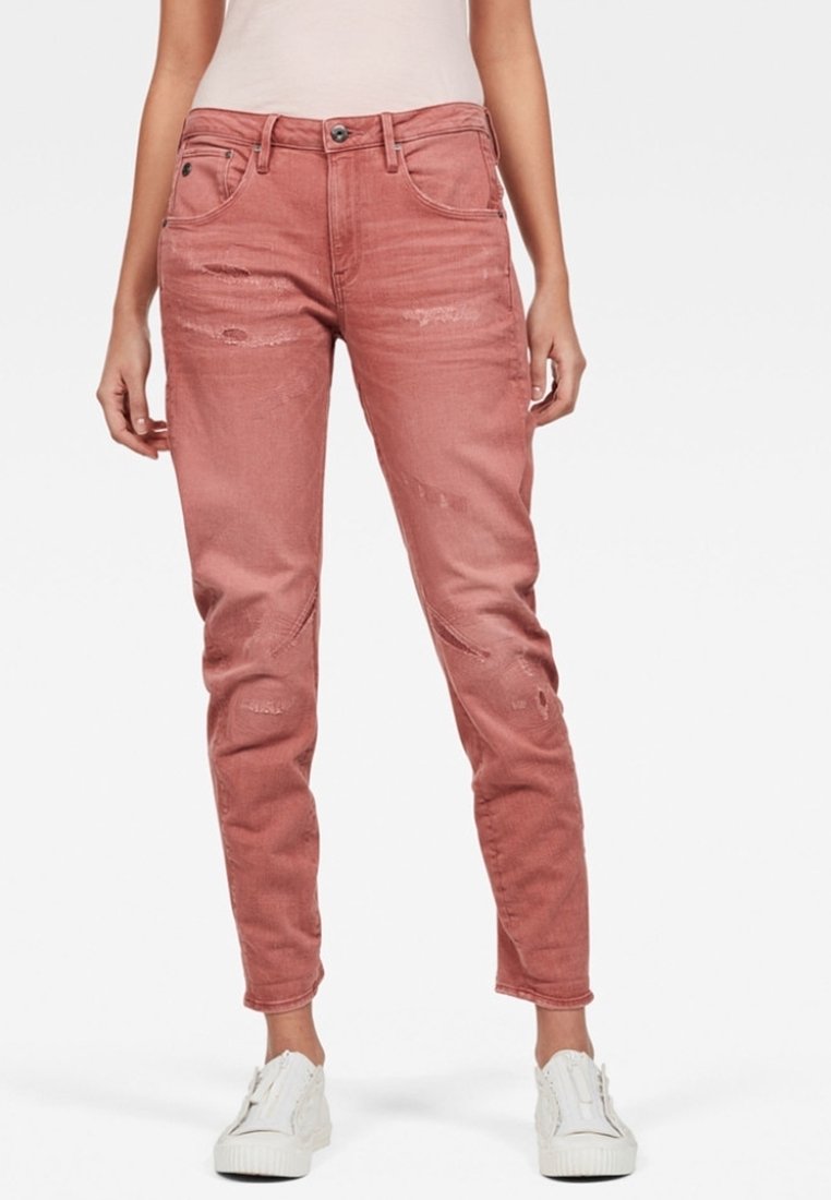 Pantalones vaqueros ajustados de mezclilla en tono rosado desgastado con parches rasgados y un diseño clásico de cinco bolsillos. Acompañados de zapatillas blancas.
