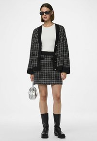 Cardigan a scacchi bianco e nero, top bianco, gonna nera aderente, stivali neri fino al ginocchio, mini borsa argentata. Tessuto liscio con dettagli di bottoni.