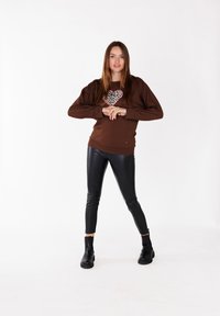 Bruine sweatshirt met een luipaardprint hartontwerp, gecombineerd met zwarte leren leggings en enkellaarsjes, met een getailleerde pasvorm.