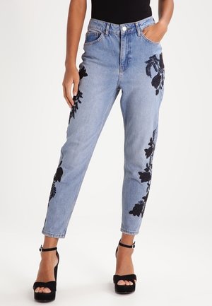 Vaaleansiniset farkut, joissa on musta kukka-allas brodeeraus sivuilla, korkea vyötärö, kapeneva lahje ja klassinen viisi-taskuinen muotoilu.