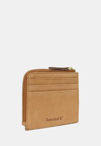 Portafoglio in pelle tan con superficie texturizzata, dotato di chiusura con zip, quattro scomparti per carte e logo Timberland stampato.