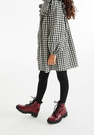 Robe à carreaux noir et blanc avec des accents froncés, associée à des collants noirs côtelés et des bottes laquées bordeaux à lacets.