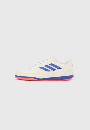 Chaussure de sport blanche et bleue avec une tige texturée, affichant trois rayures bleues, un accent rose et une semelle orange axée sur l'adhérence.