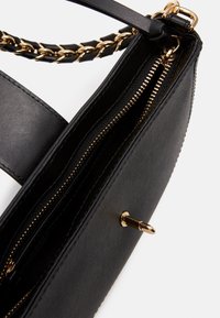 Sort syntetisk håndtaske med guldhardware, der har en flettet kædestrop og indvendige lynlåslommer. Glat tekstur, rektangulær form.