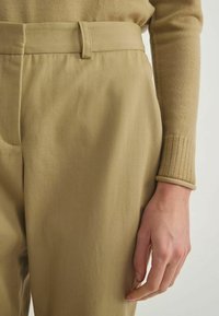 Pantalons kaki avec une texture lisse, présentant une coupe ajustée, des détails cousus, une passante de ceinture et une manche slim avec poignet en tricot côtelé.