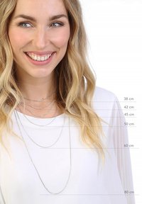 Des colliers superposés en argent de longueurs variées (38 cm, 42 cm, 45 cm, 50 cm, 60 cm, 80 cm) portés par un modèle portant un haut blanc.