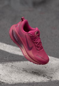 Nike bėgimo batai ryškiai rožinės spalvos su tekstūruotu paviršiumi, kontrastinga tamsiai rožine logo ir pusiau permatomu padu. Yra orui pralaidaus tinklinio dizaino.