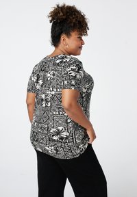 Zwart-wit gestreepte top met korte mouwen, voorzien van bloem- en geometrische ontwerpen, gecombineerd met zwarte broek, weergegeven vanaf de zijkant.
