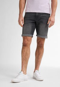 Pantalones cortos de mezclilla gris con dobladillo vuelto, con un diseño de corte ajustado. Llevados con zapatillas blancas y una camiseta de color rosa claro.