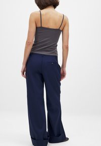 Top de tirantes gris combinado con pantalones de pierna ancha navy. Los pantalones cuentan con un bolsillo trasero con botón, una textura suave y un ajuste diseñado.