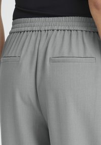 Grå afslappede bukser med elastik i taljen og to baglommer. Glat tekstur, letvægtsstof og et skræddersyet design.