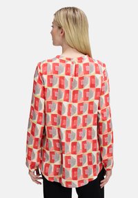 Langärmlige Bluse aus einem weichen, leichten Stoff mit einem geometrischen Muster in Rot, Grau, Gelb und Beige, mit rundem Halsausschnitt und Falten-Detail.