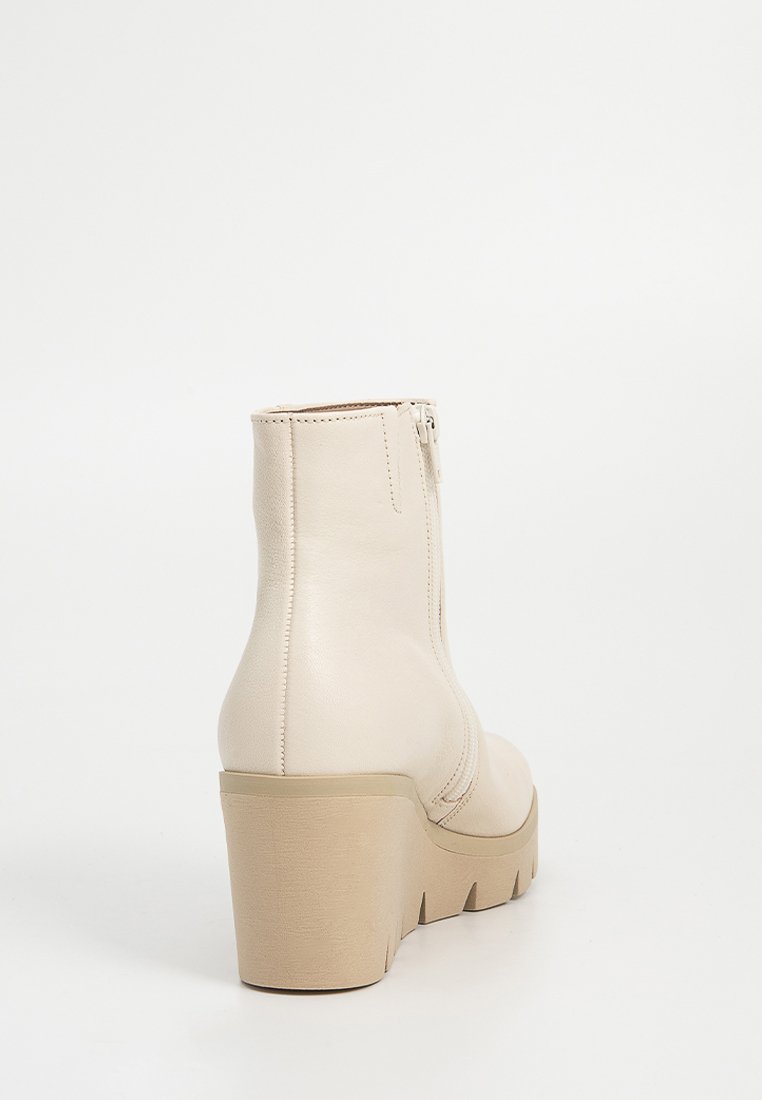 Crème-kleurige enkelboot met chunky hak, rits aan de zijkant en gestructureerde zool, gefotografeerd tegen een eenvoudige witte achtergrond.