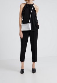 Haut noir à bretelles avec volants, pantalon noir ajusté, et sac bandoulière argenté brillant. Chaussures à talons noires fermées complètent le look.