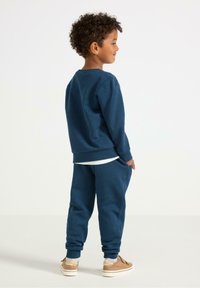 Dunkelblaues Sweatshirt- und Hosen-Set für Kinder, aus weichem Stoff. Die Hose hat seitliche Taschen und Bündchen, getragen mit hellen Schuhen.