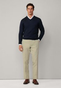 Marineblauer V-Ausschnitt-Pullover, hellbeige Hose, braune Slipper, mit einem weißen Hemd darunter; glatte Textur, taillierte Passform.