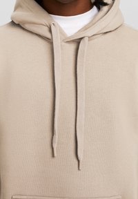 Felpa con cappuccio beige in materiale morbido con tasca a marsupio frontale, coulisse e polsini a costine, caratterizzata da una vestibilità comoda.