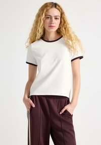 Kortærmet hvid T-shirt med en burgunder rund hals og ærmekant, parret med burgunder bukser med sidelommer og striber.