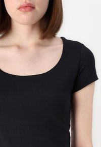 Čierne, priliehavé tričko s okrúhlym výstrihom a krátkymi rukávmi. Hladká tkanina s jemným leskom, zdôrazňujúca minimalistický dizajn.