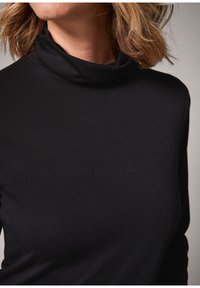 Haut à col roulé noir en tissu doux et extensible. Caractérisé par un col montant et une coupe ajustée, idéal pour être porté en superposition ou seul.