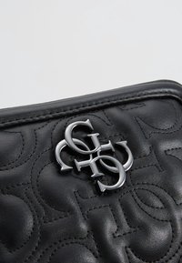 Czarna pikowana skórzana torebka z metalowym akcentem logo. Zaokrąglone krawędzie i gładka tekstura z przeszyciem.