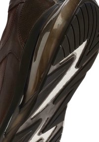 Zapato de cuero marrón con suela de goma que presenta un agarre texturizado, diseño curvado y elegantes detalles a lo largo de los lados y el tacón.