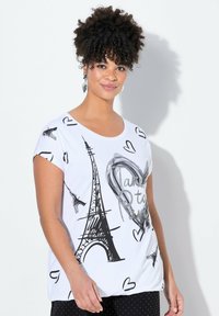 Camiseta blanca de manga corta con estampados en negro de la Torre Eiffel y corazones, con un texto decorativo en plateado. Tejido suave con un corte relajado.