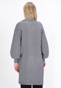 Graues, übergroßes Strickkleid mit strukturiertem Finish, langen Puffärmeln und einem Kragen. Endet oberhalb des Knies mit einer lockeren Passform.