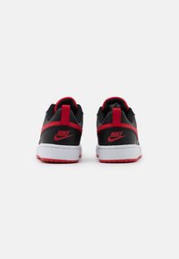 Black sneakers with red accents, featuring a smooth synthetic upper, padded collar, and prominent Nike logo on the heel. White midsole with red outsole.