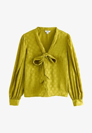 Blusa verde con scollatura a V, dettaglio con fiocco frontale, maniche lunghe a sbuffo e motivo a pois; realizzata in tessuto leggero e strutturato.