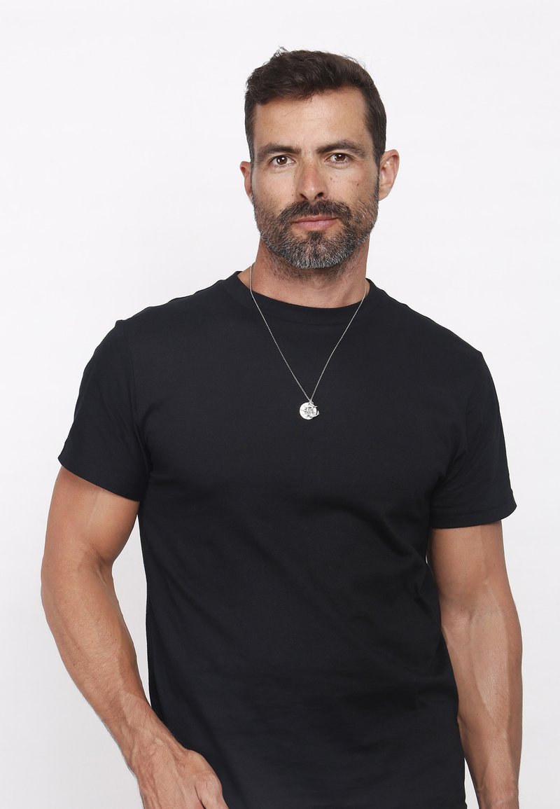 Schwarzes Baumwoll-T-Shirt mit kurzen Ärmeln, rundem Halsausschnitt und figurnaher Form; enthält eine silberne Halskette mit einem runden Anhänger.