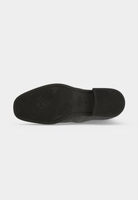 Semelle en caoutchouc d'une chaussure habillée pour homme avec des motifs antidérapants texturés et le nom de la marque « GANT » embossé près de la voûte plantaire.