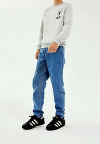 Šedá mikina s černou grafikou, světle modré džíny a černé tenisky s bílými pruhy. Neformální oblečení, jednoduchý design.