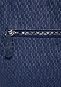 Nahaufnahme eines dunkelblauen strukturierten Stoffes mit einem horizontalen silbernen Reißverschluss und einer Leder-Reißverschlusslasche.