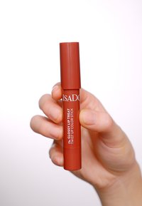 Matita labbra rossa a torsione tenuta in mano, etichettata "ISADORA The Glossy Lip Treat." Superficie liscia, forma cilindrica, finitura lucida.