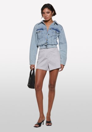 Veste en denim de couleur bleu clair avec deux poches poitrine, assortie à un short gris clair. Un sac à main noir et des talons ouverts noirs complètent le look.
