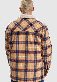 Flannel shirt, tan with blue and red check pattern, soft texture, buttoned cuffs, and shearling collar. Back view showing plaid design.