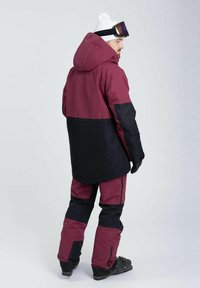 Skijakke og -bukser i bordeaux og sort, med hætte, justerbare elementer og vandtæt materiale. Reflekterende detaljer på bukserne.