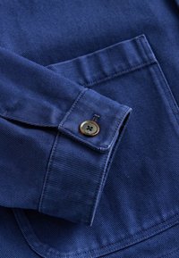 Marineblåt skjortestof med en lodret ribbet struktur, med manchet med knapper og en brystlomme. Enkel design med rene linjer.