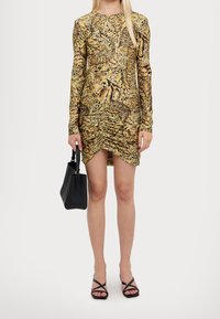 Långärmad, figurnära klänning med ett djurmönster i guld- och bruntoner, med ruching vid fållarna. Matchad med en svart handväska och sandaler.