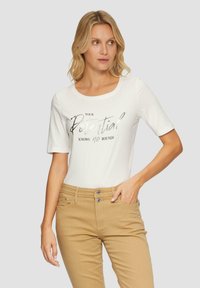 Witte katoen t-shirt met korte mouwen met een metallic zilveren opdruk die zegt "Jouw potentieel kent geen grenzen." Gecombineerd met kaki broek.