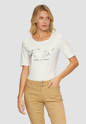Witte katoen t-shirt met korte mouwen met een metallic zilveren opdruk die zegt "Jouw potentieel kent geen grenzen." Gecombineerd met kaki broek.