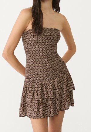 Robe marron sans bretelles avec motif floral beige, corsage ajusté smocké et jupe à volants superposés portée par une femme aux longs cheveux foncés.