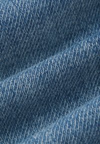 Denim w klasycznym niebieskim kolorze, ukazujący teksturowany splot z różnorodnymi odcieniami i diagonalnymi liniami. Gładka powierzchnia o miękkim wyglądzie.