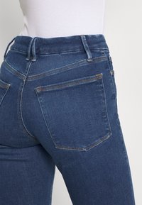 Jeans de mezclilla azul oscuro con un diseño ajustado, que cuentan con bolsillos traseros y costuras en contraste, mostrados desde la cintura hasta el área del muslo.