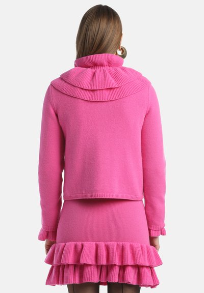 Suéter de punto de color rosa brillante con un cuello con volantes, combinado con una falda a juego con un dobladillo con volantes. Ambos tienen una textura suave y un diseño ajustado.