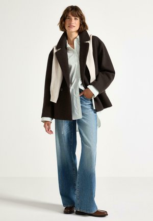 Brun och krämfärgad oversized ullblandad kappa, matchad med en ljusblå randig skjorta och vida, utblekta jeans. Accentuerad med bruna stövlar.