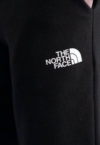 Zwarte stof met een wit logo van "The North Face" met een gebogen bergontwerp aan de linkerkant. Glad textuur, aansluitend ontwerp.