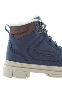 Mörkblå ankelskor med fuskpälsfoder, bruna accenter, metallöglor och en kraftig beigefärgad sula. Har varumärket U.S. Polo Assn.